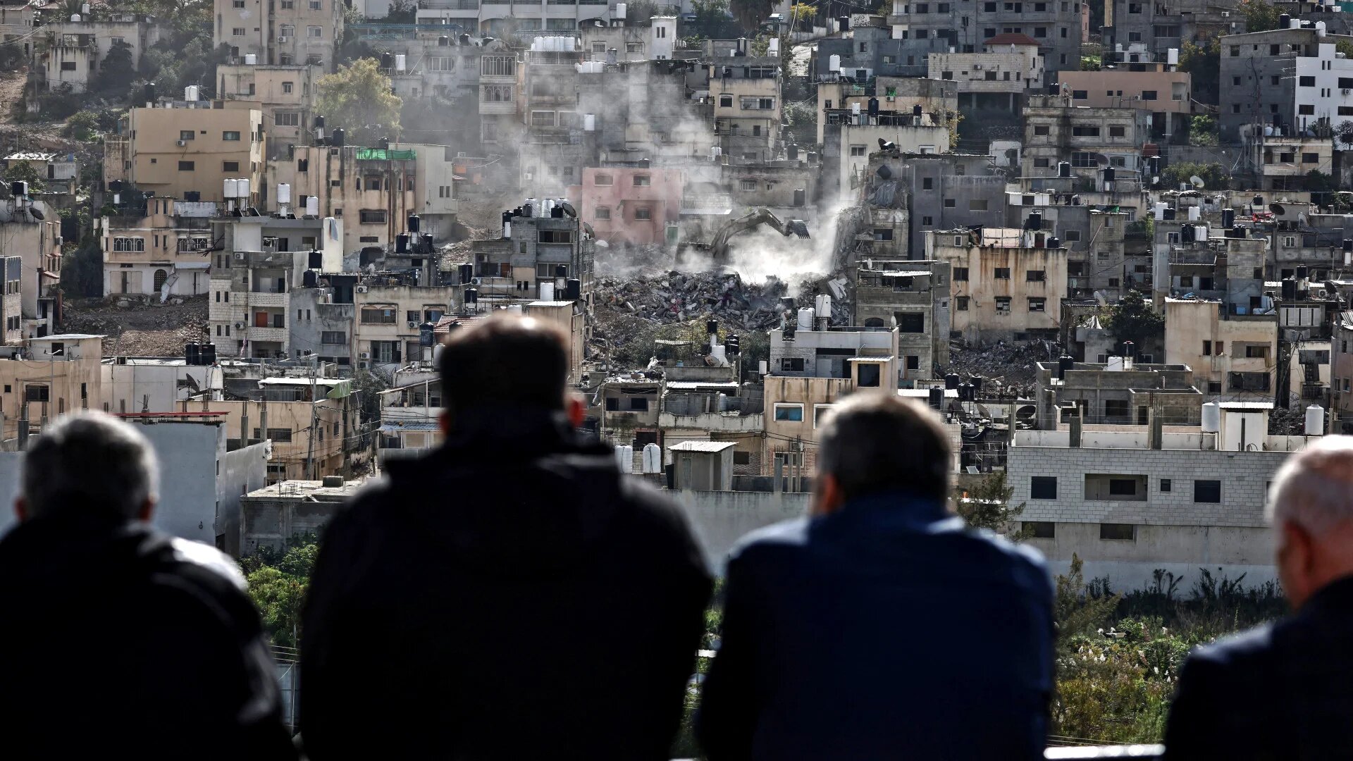 Residents of the Nur Shams refugee camp watch as an Israeli military excavator demolishes their homes on New Year's Eve, east of Tulkarm in the northern Israeli-occupied West Bank, during ongoing Israeli offensives, on 31 December 2025 (Zain Jaafar/AFP)