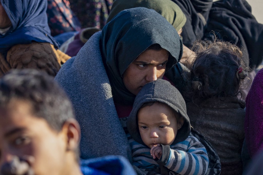 A Syrian Kurdish woman, fleeing from north of Aleppo, holds a child as she waits with others upon their arrival in Tabqa, on the western outskirts of Raqa, on December 4, 2024