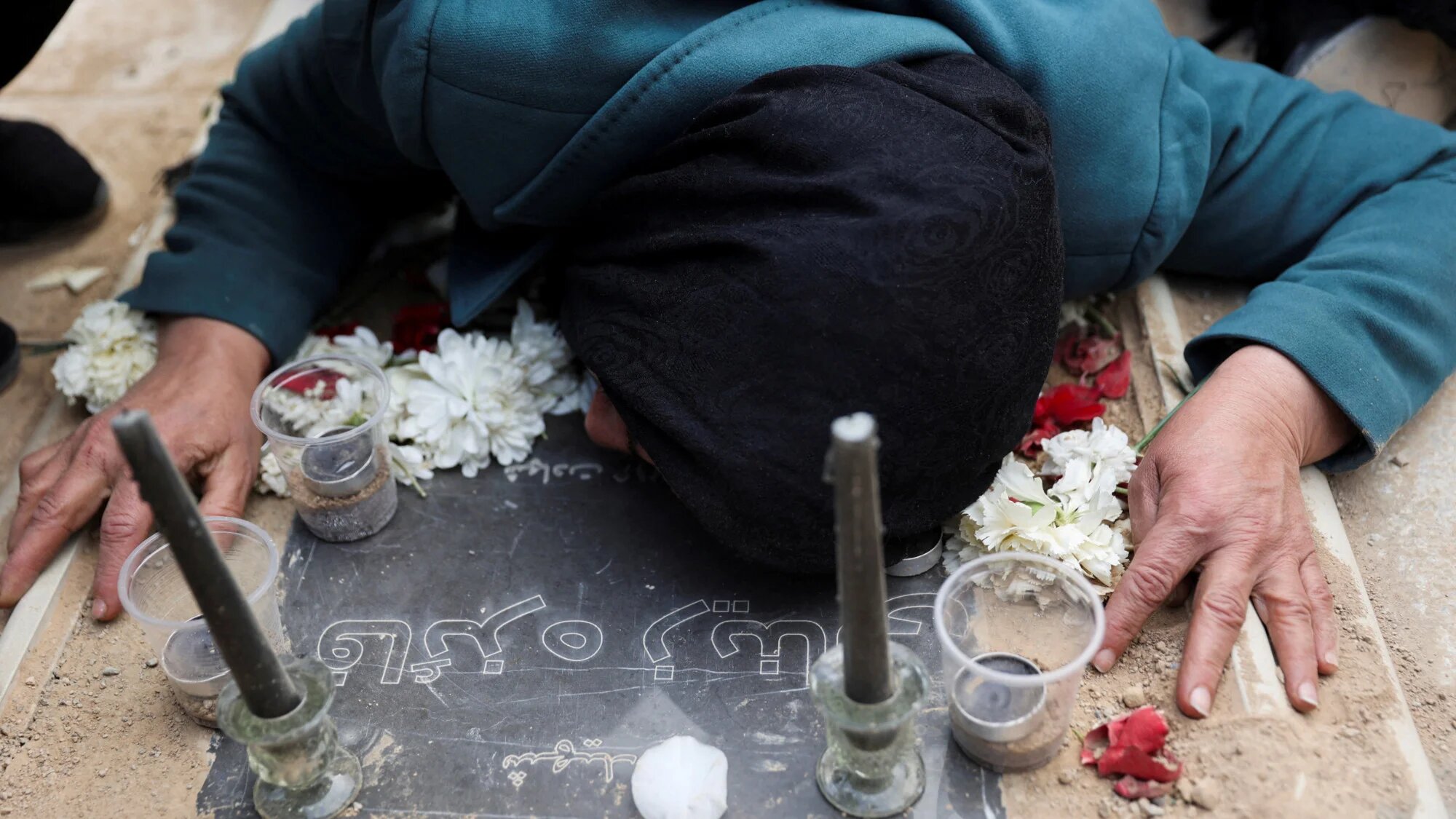 A mourner lies on a grave as she attends a funeral ceremony for victims of Israeli and US strikes, in Tehran, 9 March 2026 (Wana/Reuters)