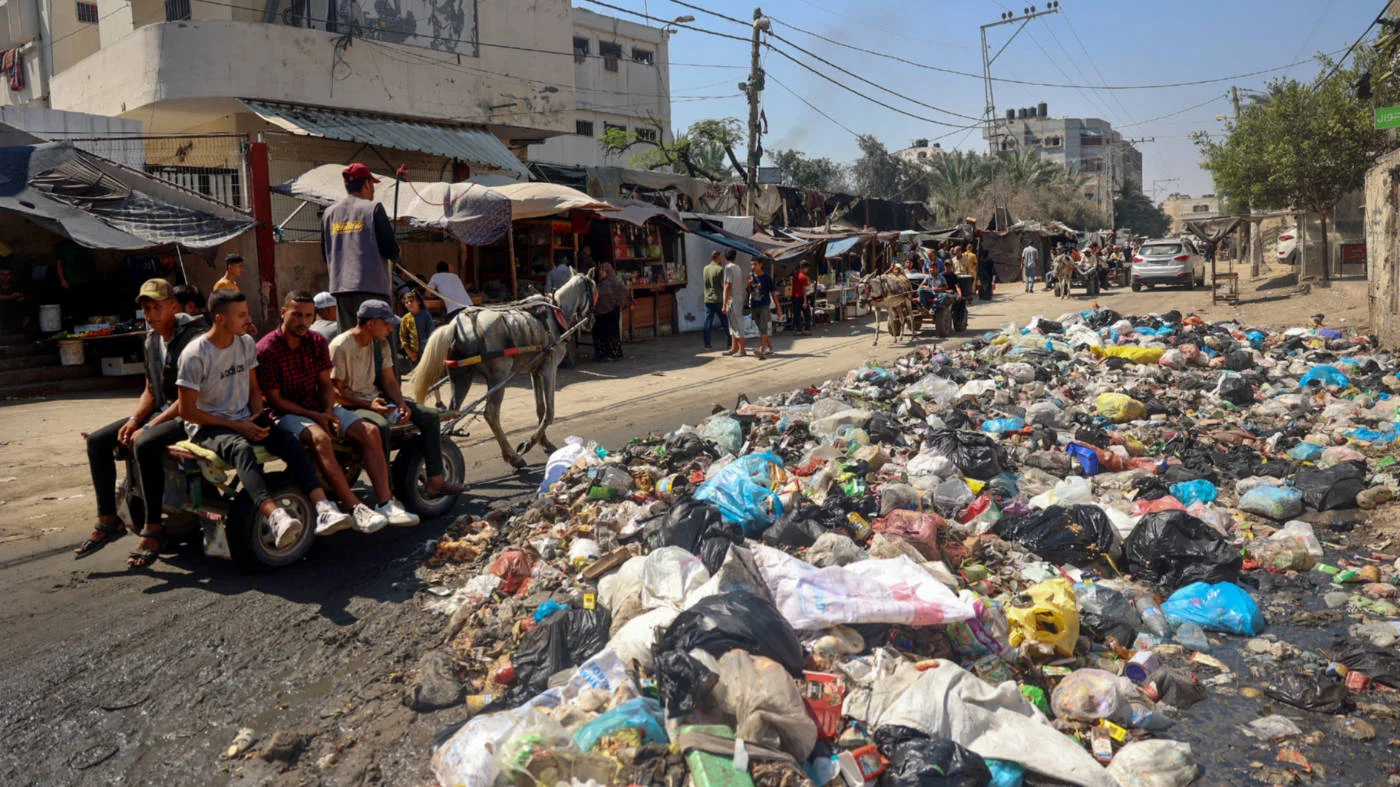 Palestinians ride a donkey-drawn cart past a garbage dump and sewage water on a street in Deir el-Balah in July 2024 (AFP)